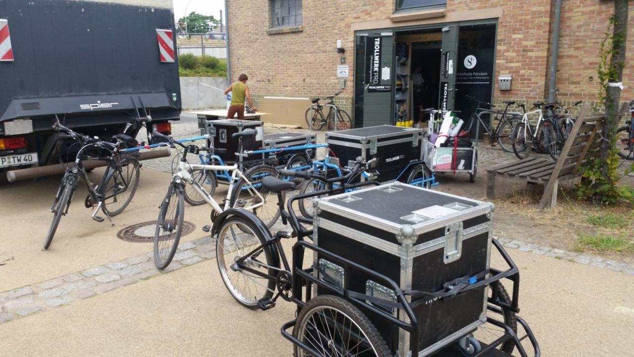Ein Lastenfahrrad und zwei Fahrräder mit jeweils einem großen Anhänger sind mit großen Kisten (Cases) beladen.