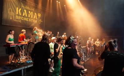 Foto von einer Bühne, ein Banner vom KAMA-Orchester ist zu sehen und Scheinwerferlicht kommt von oben.